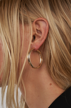 A woman is wearing gold hoop earrings, available at www.shopriseonline.com